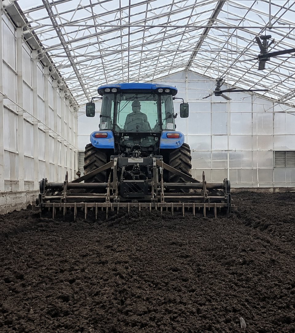 Biosolids composting operation with heavy equipment moving dark organic material inside a covered facility.