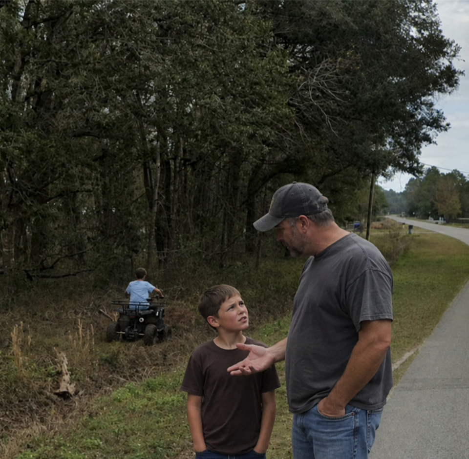 A father explains something to his confused son while another child rides a four-wheeler through a Flagler Estates drainage ditch behind them.