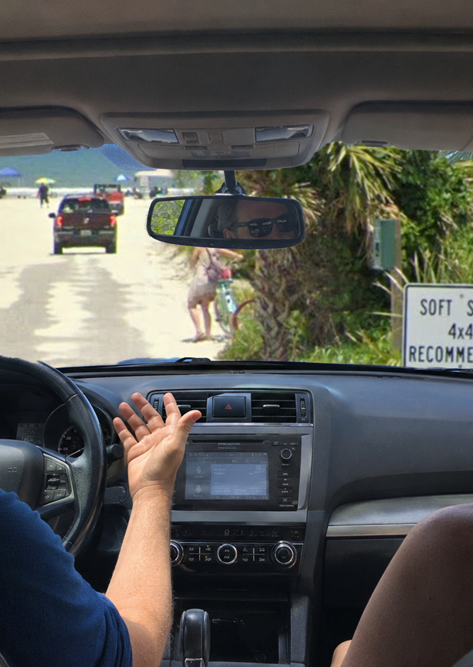 View from inside a Subaru at a St. Augustine Beach vehicle entrance as the husband gestures, his wife points toward a “Soft Sand 4x4 Only” sign and a Jeep drives ahead.