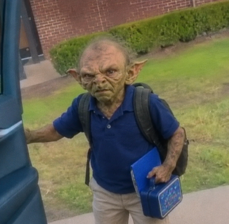 A young student wearing a blue polo and backpack holds a lunchbox and binder while getting out of a car on the first day of school.